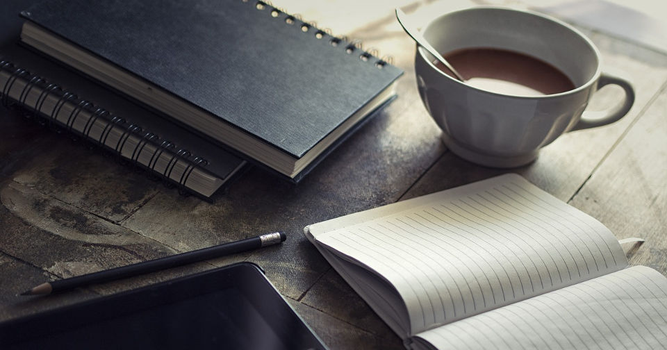 Leżące na biurku notatniki, ołówek i filiżanka z kawą